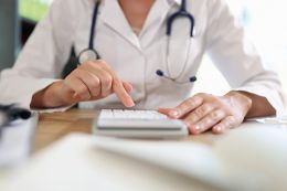 Foto: Ärztin arbeitet auf Taschenrechner im Büro